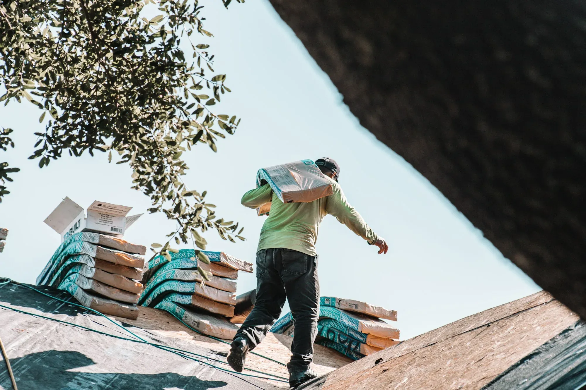 Roofer carrying a bundle of shingles across a house roof during a roof replacement